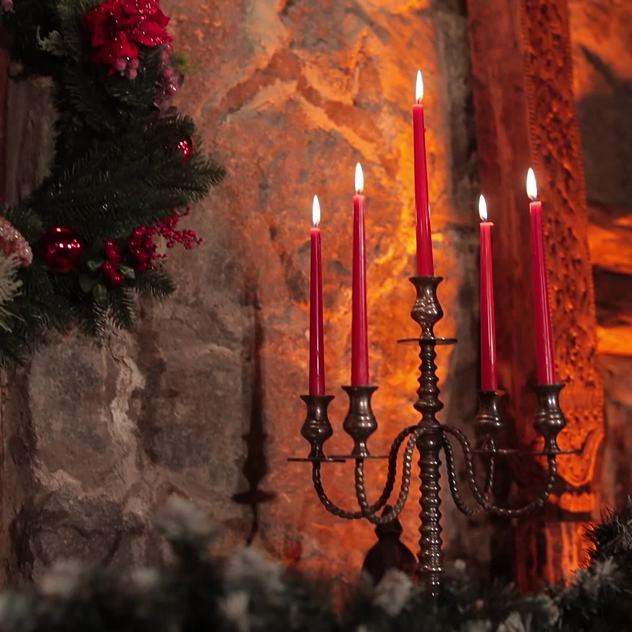 Christmas wreath with red flowers and berries hanging on the stone wall. Red burning candles on the silver candlestick