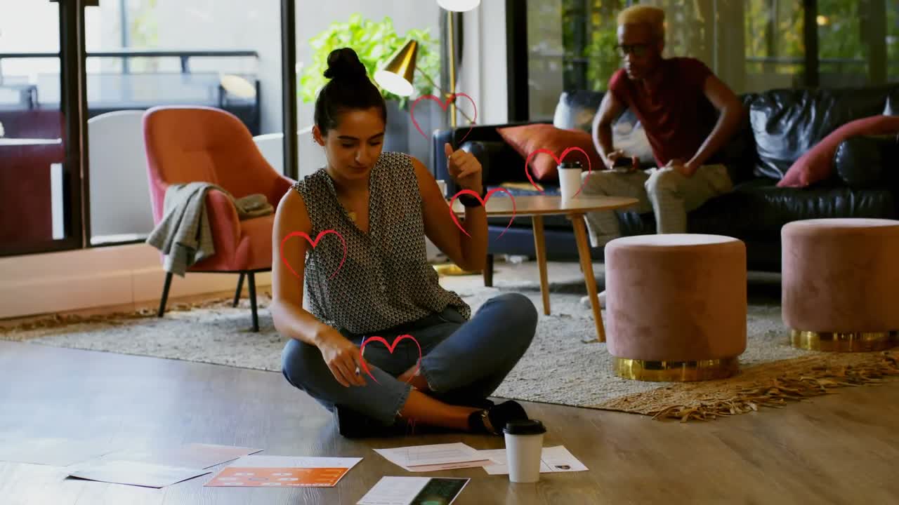 Animation of red heart icons over diverse male and female colleagues discussing over documents