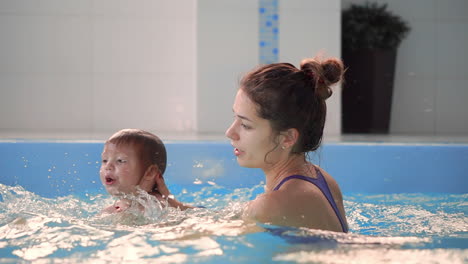 beautiful mother teaching cute baby girl how to swim in a swimming pool. child having fun in water with mom.