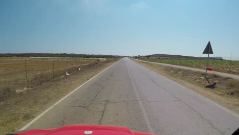 punto de vista conduciendo por una carretera pavimentada que pasa por tierras de cultivo en chipre y un pequeño puesto de frutas al borde de la carretera