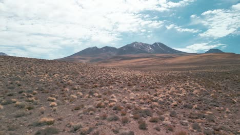 Drone-Volando-Cerca-De-La-Tierra-Seca-Del-Desierto-Chileno-Con-Un-Volcán-En-El-Fondo