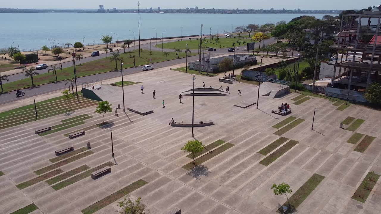 Alejamiento amplio de dron de niños en un parque de patinaje con el océano azul de fondo.