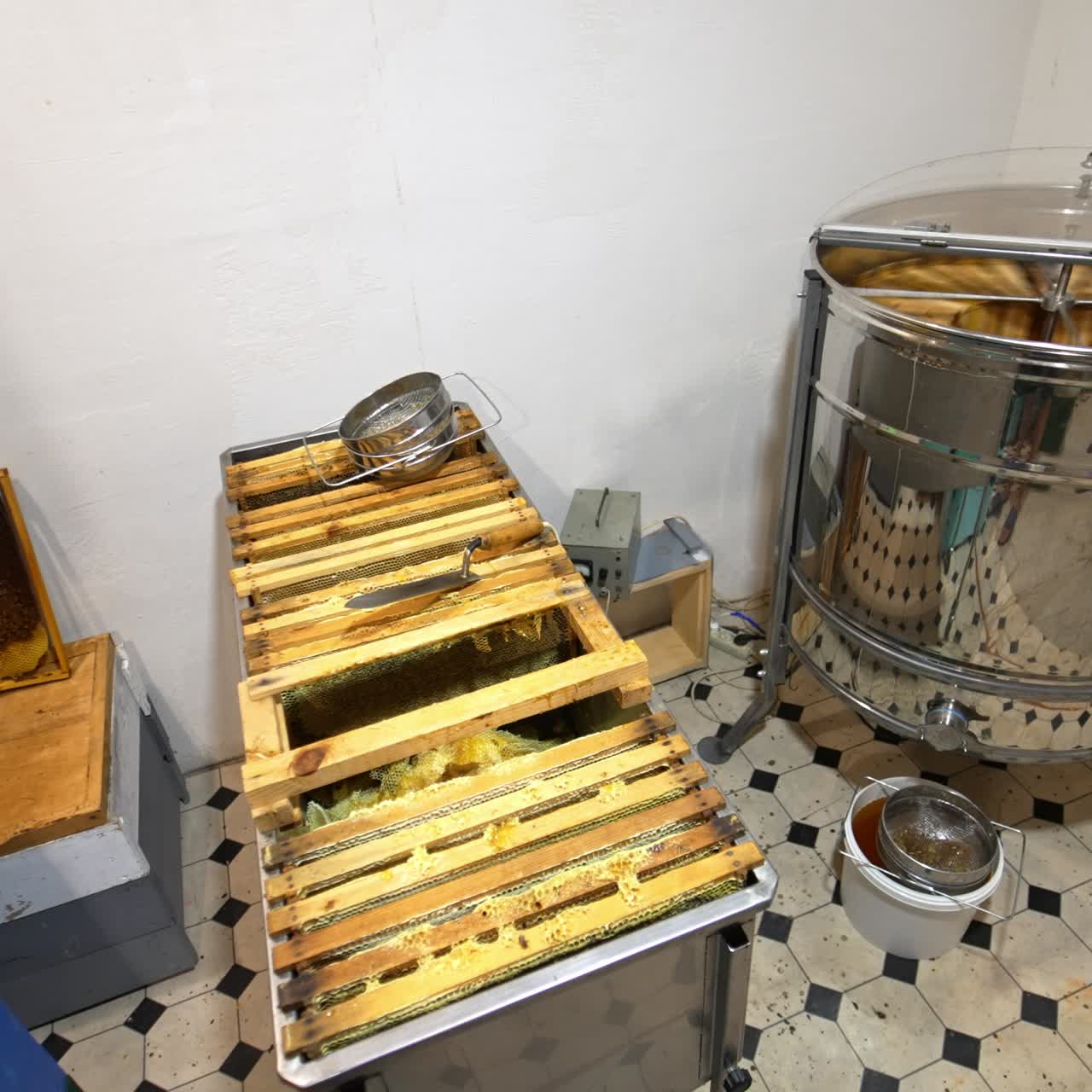 Small room with working honey extracting machine. Large metal box of frames waiting for pumping beside the centrifuge. High angle view