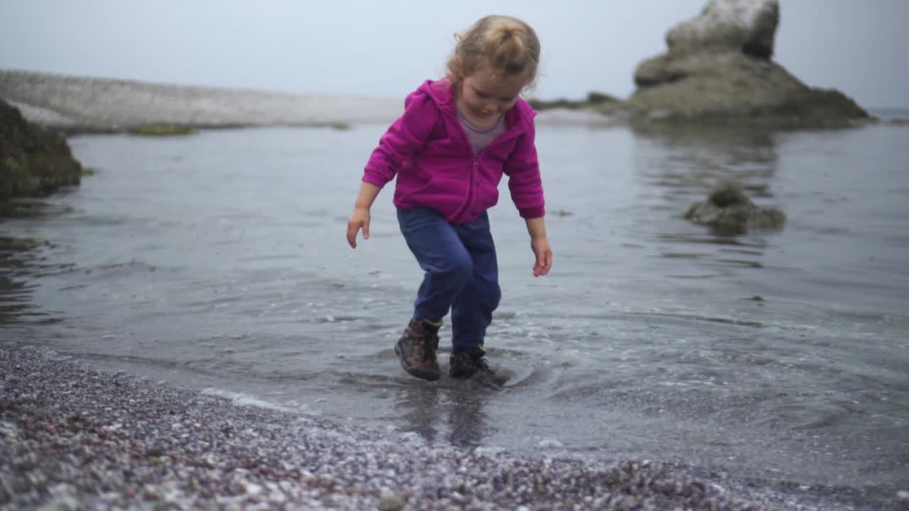 adorable niñita a la orilla del mar jugando al agua con las manos y los pies y luego se aleja - plano medio