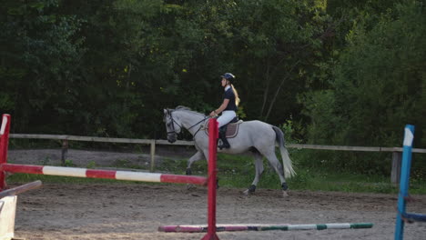 professional girl rider galloping on a horse. girl riding a horse on an arena at sunset. horse hoof creates a lot of dust. competitive rider training jumping.