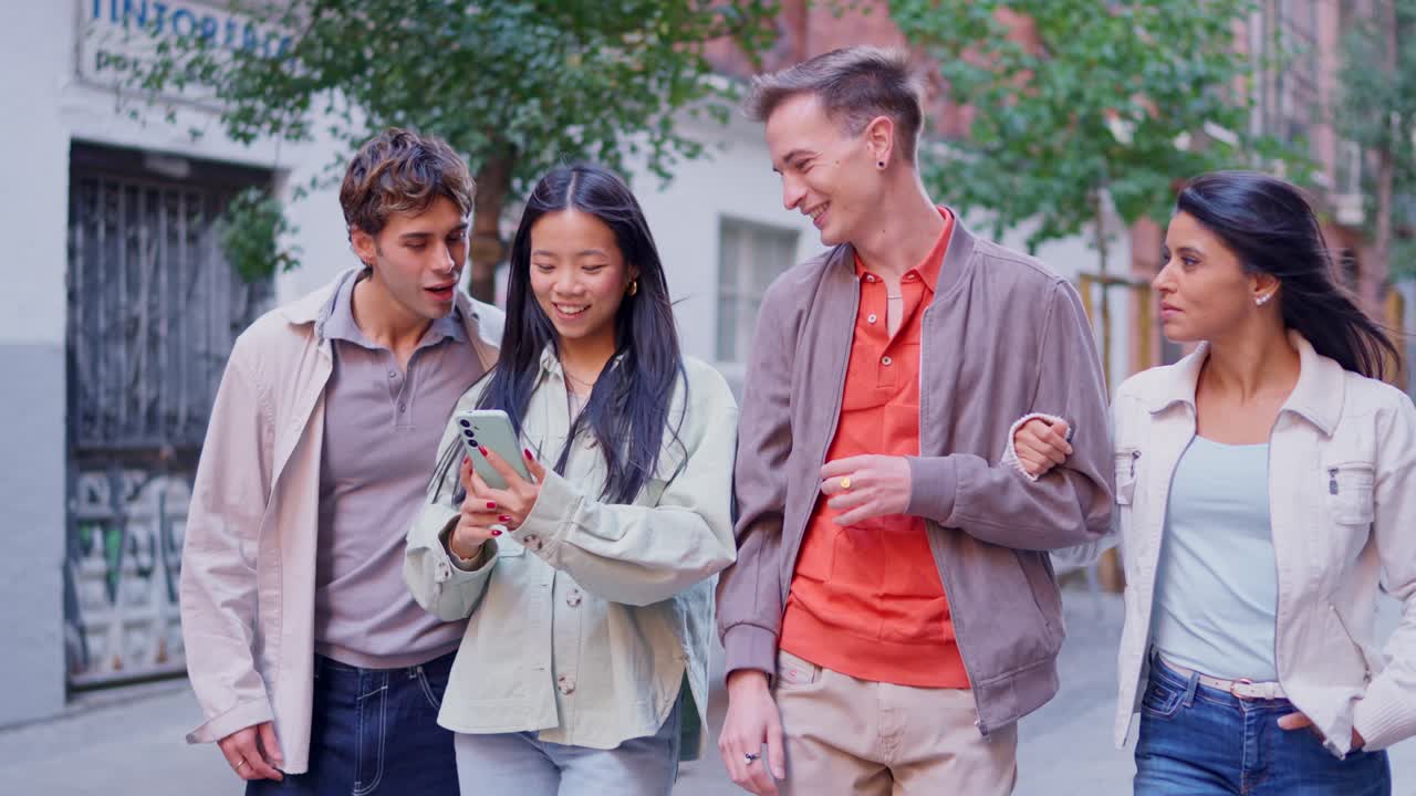 Giovani amici felici che camminano e guardano lo smartphone per le vie della città