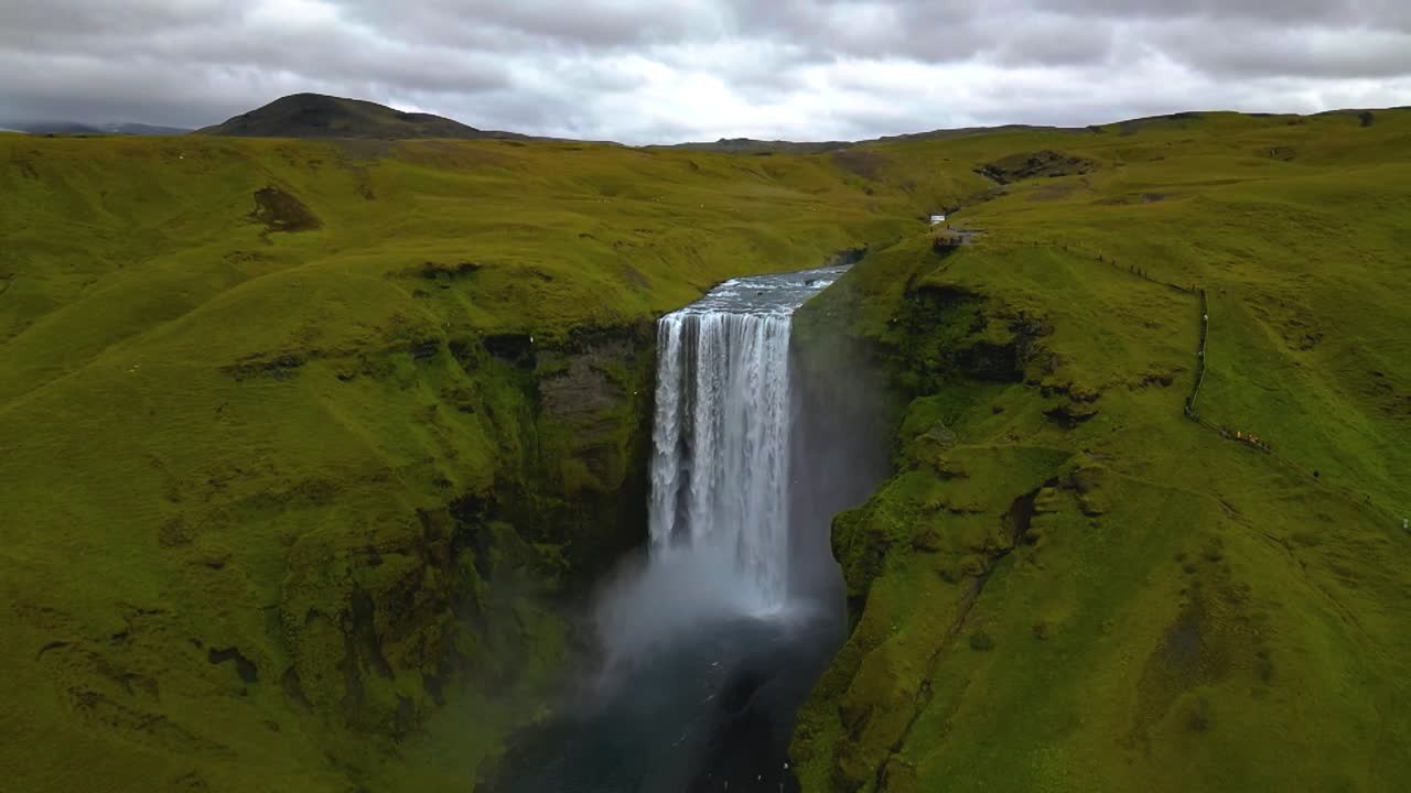 4K cinematic drone footage of Skógafoss Waterfall in Iceland, capturing the immense curtain of water cascading from towering cliffs surrounded by lush green landscapes. Iceland_24