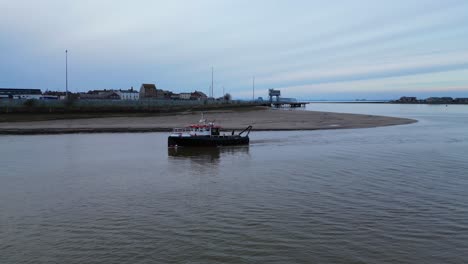 Small-boat-entering-harbour-on-calm-water-at-dusk-on-the-River-Wyre-Estuary-Fleetwood-Lancashire-UK