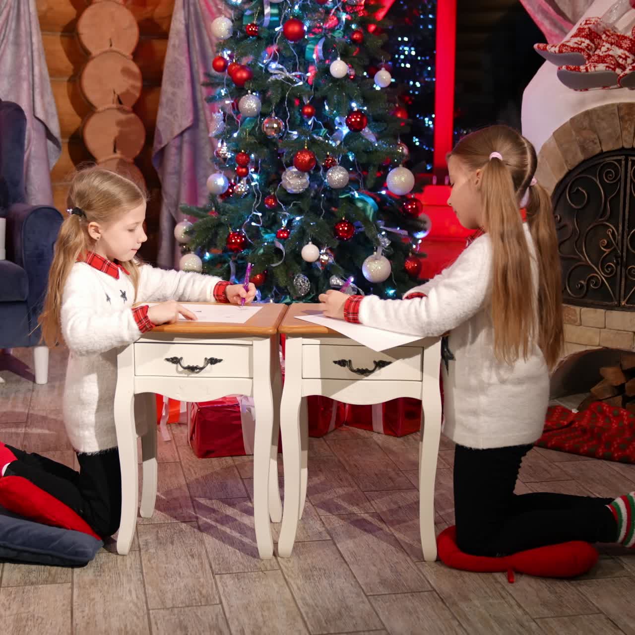 Children painting at Christmas decorated room. Cute little girls sitting on floor and drawing pictures on small desks for Santa. Christmas spirit