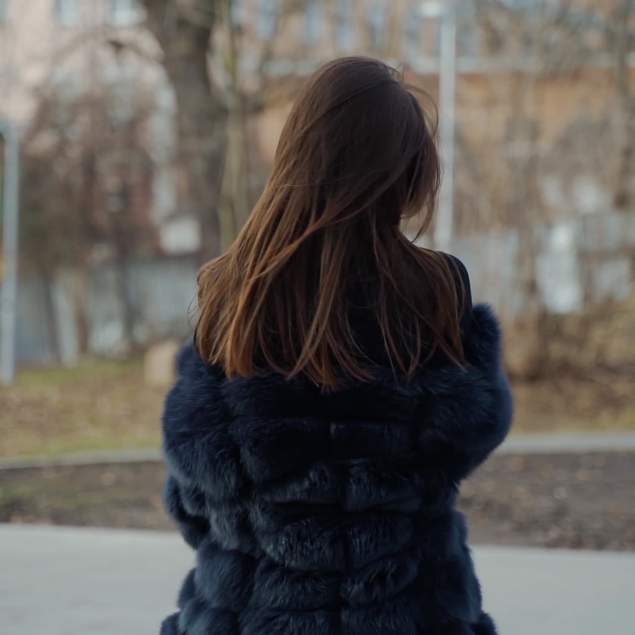 Young beautiful fashionable lady wearing stylish dark fur coat posing in park. Model looking aside. Female fashion concept. City lifestyle. Fashion video.