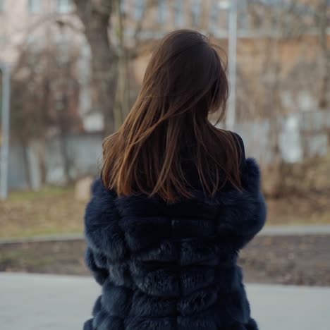 young beautiful fashionable lady wearing stylish dark fur coat posing in park. model looking aside. female fashion concept. city lifestyle. fashion video.