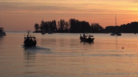 Barco-De-Pesca-Tradicional-Navegando-Hacia-Adelante,-Pescador-Hacia-El-Mar-Para-Pescar-Al-Atardecer-Con-Un-Hermoso-Cielo-Naranja-Y-Un-Reflejo-De-Aguas-Tranquilas,-Ambiente-Tropical-De-Verano-En-La-Isla-De-Langkawi,-Malasia