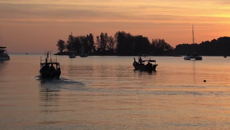 traditional fishing boat cruising forward, fisherman out to the sea to catch fish at sunset with beautiful orange sky and calm water reflection, tropical summer vibe at langkawi island, malaysia