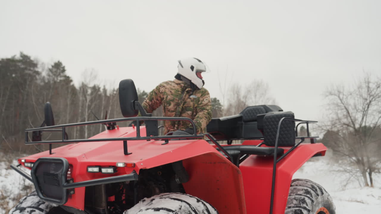 ATV rosso in campo innevato, pilota in mimetica che percorre un sentiero fuoristrada, le gomme posteriori sollevano neve, cielo coperto, sullo sfondo una pineta; un avventuriero in spedizione invernale, con raffiche di acceleratore e derapate dinamiche che ne esaltano la potenza.
