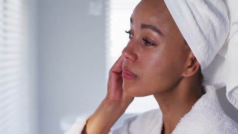 primer plano de una mujer afroamericana en albornoz limpiando su cara con un paño de algodón en el baño