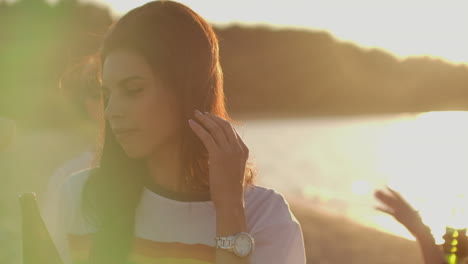 A-girl-with-long-dark-hair-in-a-short-white-t-shirt-with-a-rainbow-is-dancing-on-the-beach-party-with-her-friends.-She-touchs-her-hair-and-enjoys-open-air-party-time.