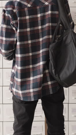 man stands in front of card index boxes in library achieve. student in checkered shirt with backpack seeks information in drawer unit. guy in paper storage