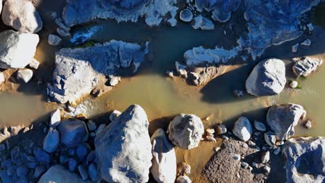 Blick-Von-Oben-Auf-Den-Fluss,-Der-An-Sonnigen-Tagen-Zwischen-Den-Felsen-Fließt