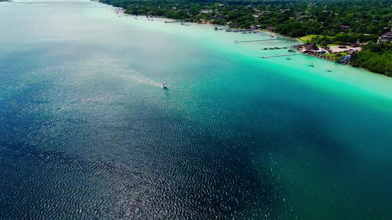 Vista aerea delle acque basse turchesi e del canale profondo della Laguna di Bacalar, Quintana Roo, Messico, con la costa verde che incornicia l'acqua calma.