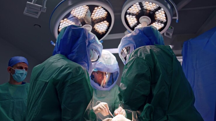 Team of three surgeons perform surgical operation wearing protective helmets. Low angle view on the surgeon using electric surgical device tool.