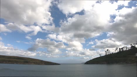 time lapse passing white clouds over water surface and blue sky with land on both sides