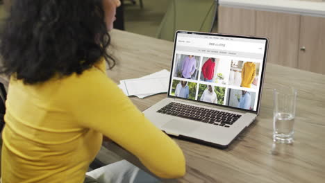 biracial woman at table using laptop, online shopping for clothing, slow motion