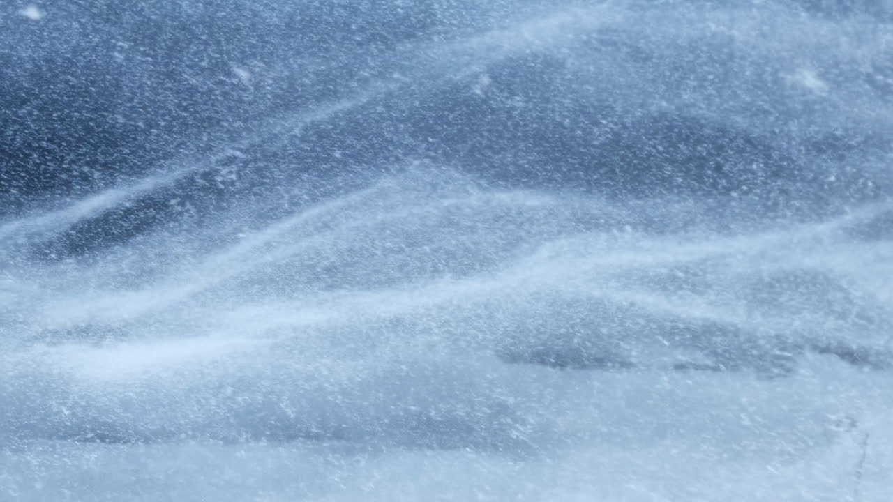 Vortici di neve blu ghiaccio che si muovono lentamente, particelle polverose che danzano in una raffica fredda, texture granulare in primo piano