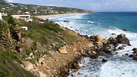 Phare-de-Camarinal,-Lighthouse
Camera-=-Static-shot-of-the-beach-with-waves-coming-in-over-rocks-that-then-pans-to-the-right-showing-rocks-and-ocean