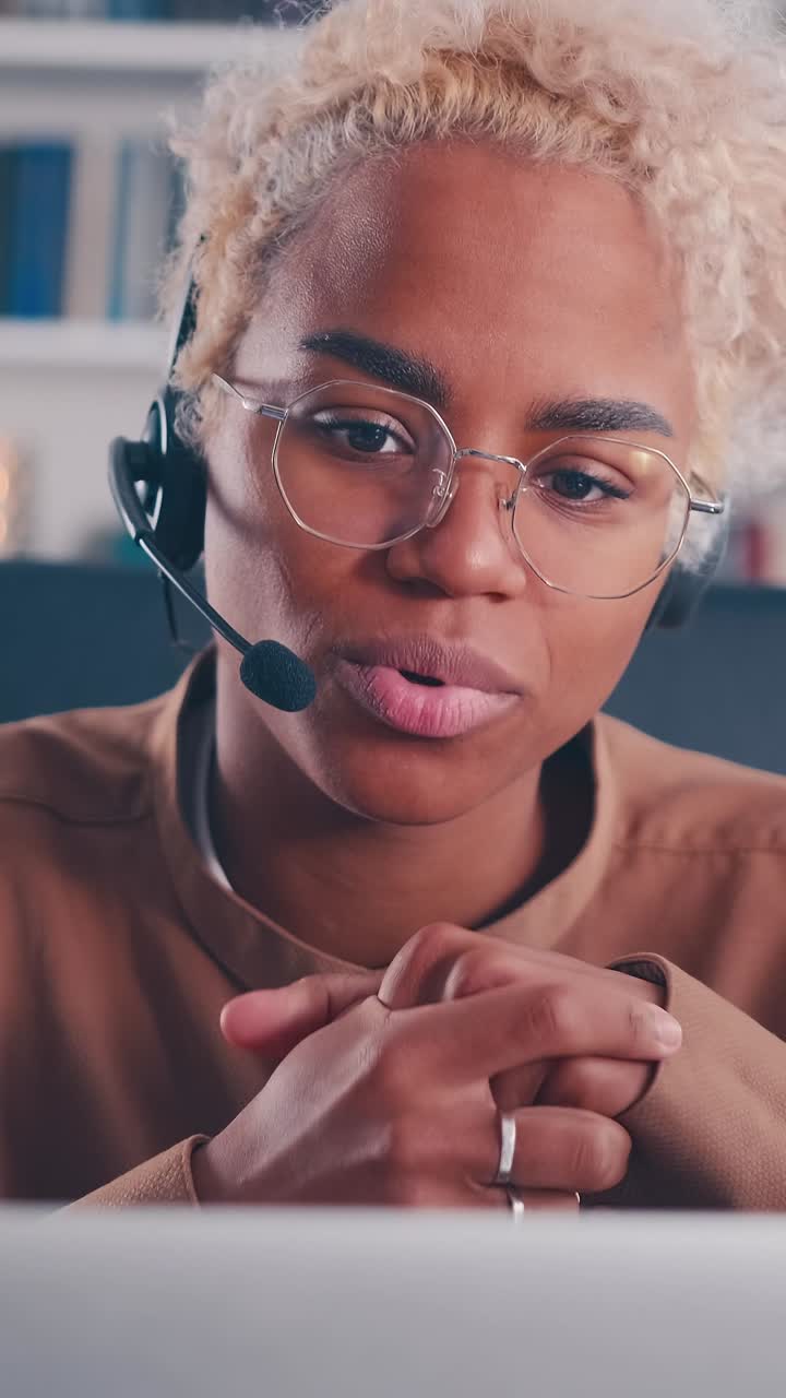 Giovane operatrice afroamericana con cuffie seduta a un tavolo con un laptop