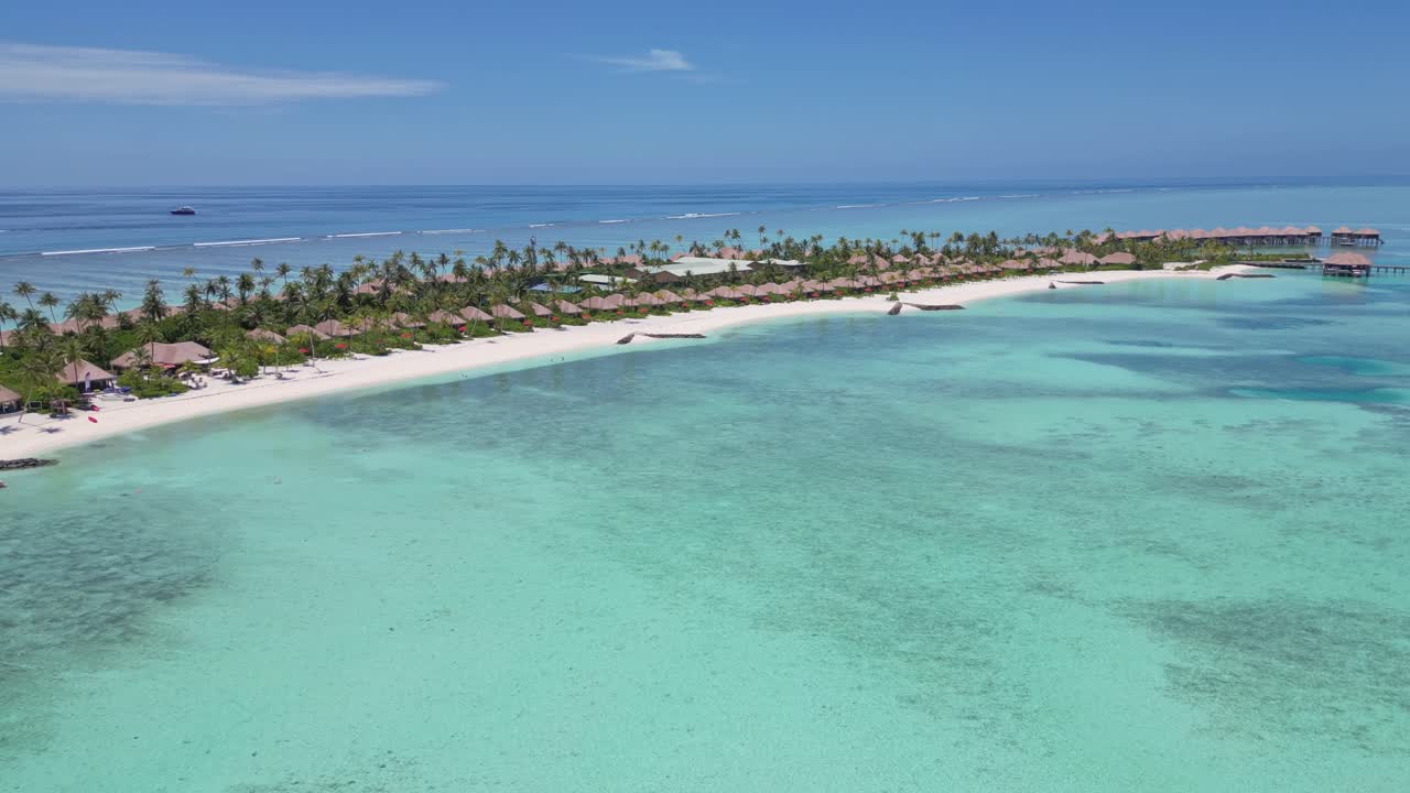 Upper class high-end waterfront villas with private sandy beach and turquoise ocean water of Maldives. Aerial backwards wide shot. Sunny summer day with blue sky. Palm trees on island.