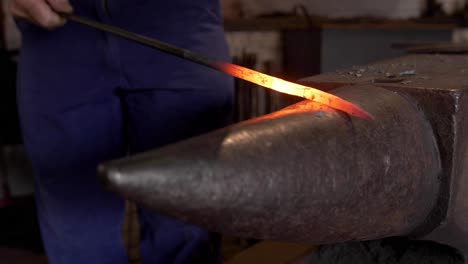 a smith forging a hot iron or steel bar on an anvil with sparks