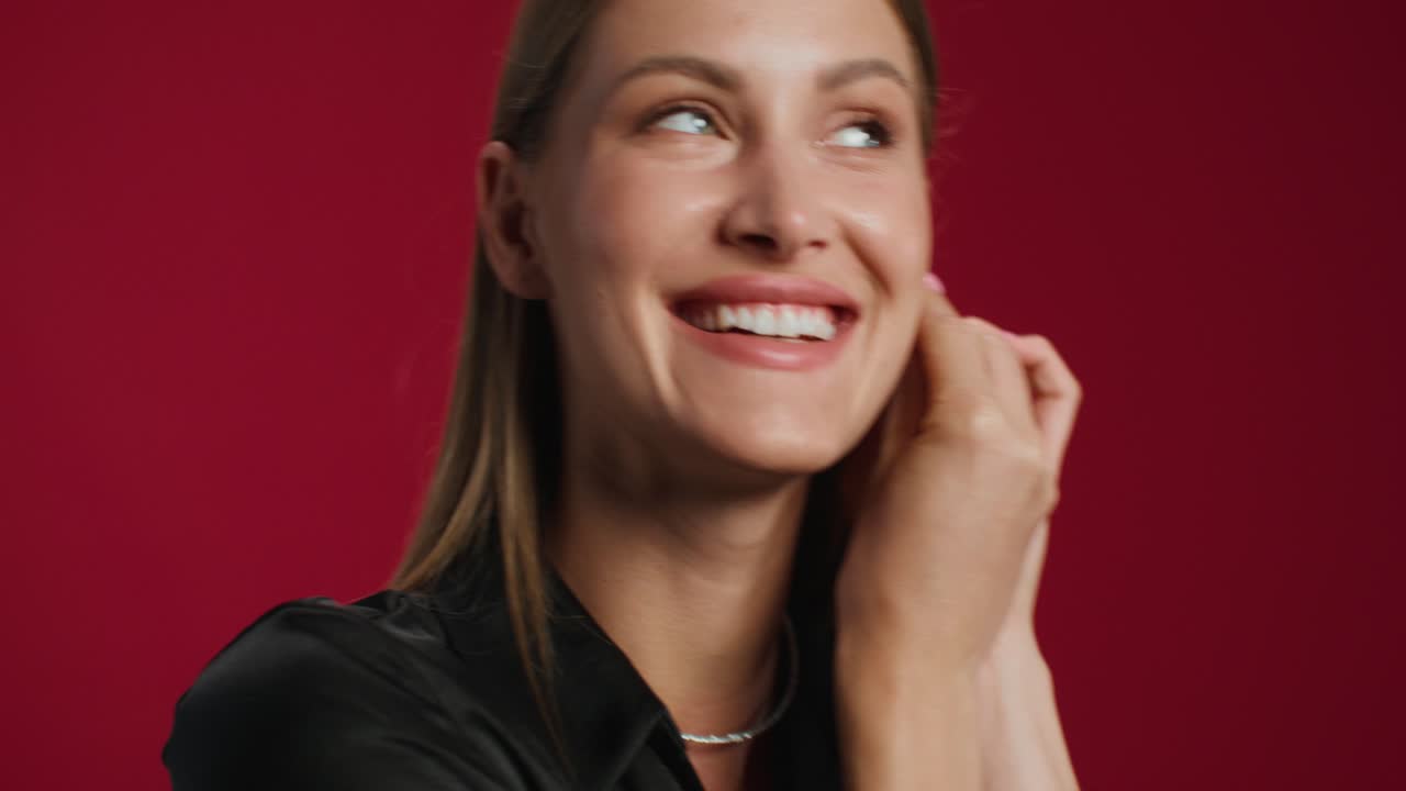 Woman Adjusting Earrings in Front of Red Background