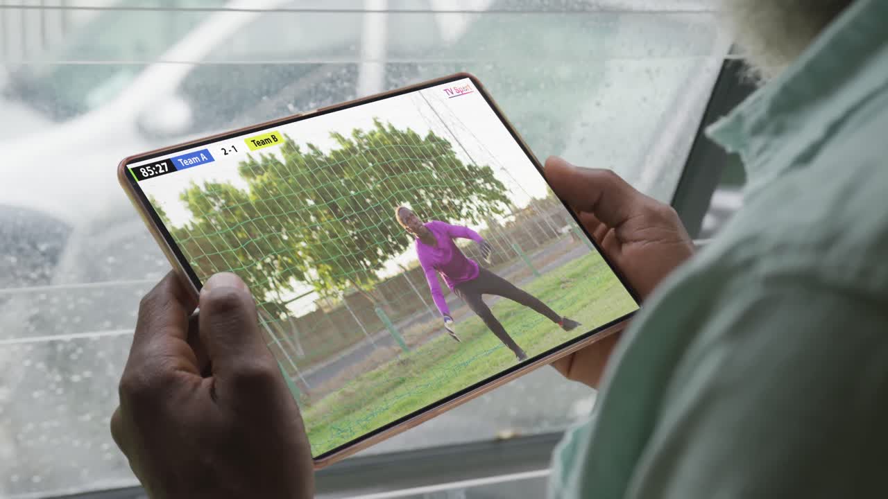 아프리카계 미국인 남자가 태블릿을 사용하고 남성 축구 선수가 화면에서 경기를 하고 있습니다.