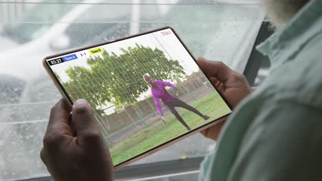 hombre afroamericano usando tableta con jugador de fútbol masculino jugando partido en la pantalla.