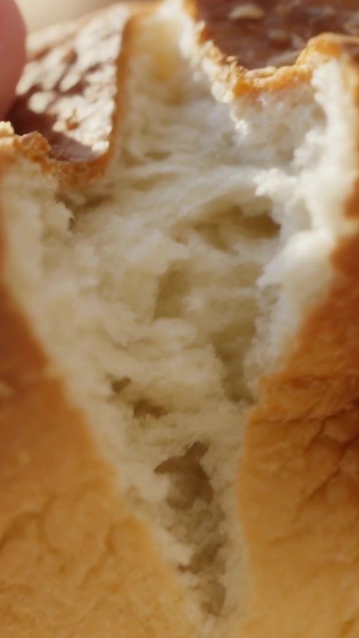 Vertical video: Pressing seam, hands pulling seeded roll apart at window, revealing crumb texture