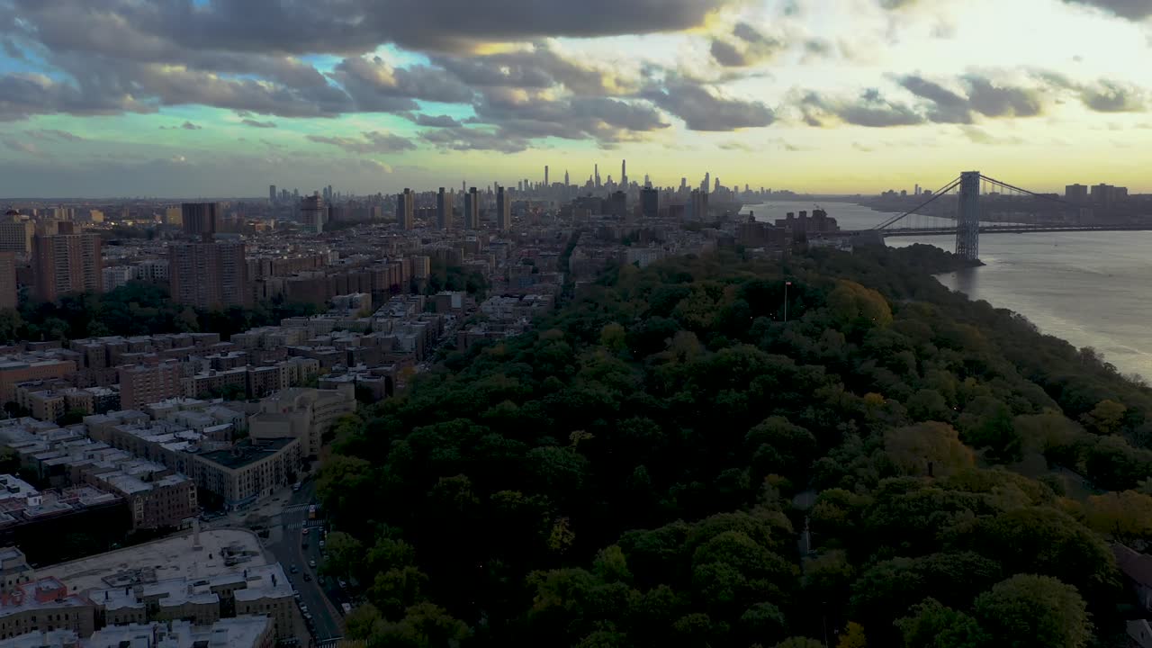 vuelo aéreo a través de la colina de inwood en la parte superior de la ciudad de manhattan nueva york con nubes dramáticas, horizonte y puente george washington en la distancia