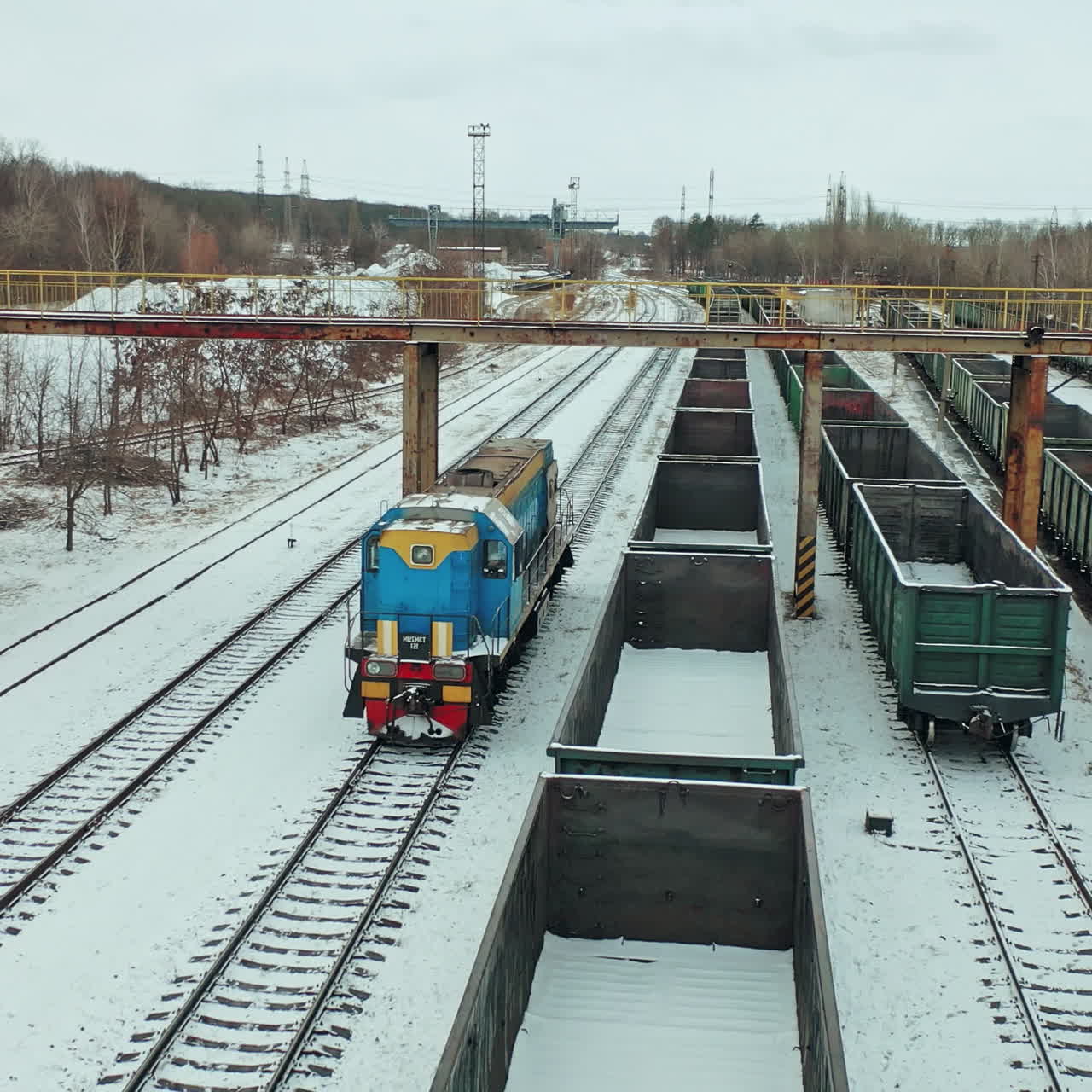 A blue freight train arrives at its destination amid a multitude of containers on a winter day. Aerial view.