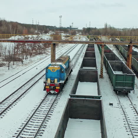 a blue freight train arrives at its destination amid a multitude of containers on a winter day. aerial view.