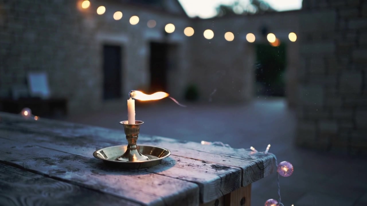 Fiamma che si piega per una folata di vento, candela di cera bianca in candeliere di ottone su tavolo di legno, con effetto bokeh.