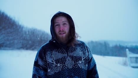 un hombre con una capucha está de pie en medio de la nieve que cae - medio de cerca