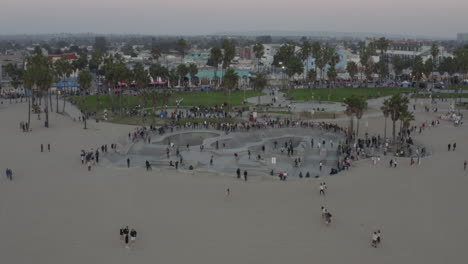 AERIAL:-Towards-Venice-Beach-Skatepark-with-Skaters-from-ocean,-Sunset,-Los-Angeles,-California