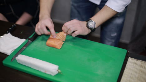 making salmon sushi, japanese food. chef is neatly cutting on fine part of salmon to make sushi