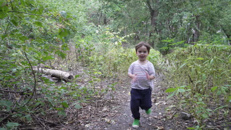child running in outdoor garden. kid runnning through the forest towards camera. steady camera shot happy young boy running alone in woods.