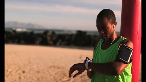 Afroamerikanischer-Männlicher-Jogger-Mit-Smartwatch-Am-Strand-In-Der-Sonne-4k