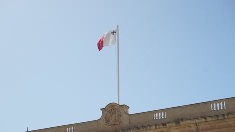 malta flag fluttering on a pole on top of building, waving in strong wind
