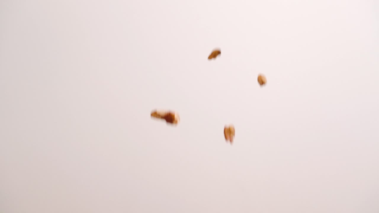 Noci pecan che piovono e rimbalzano su sfondo bianco, noci intere e a metà, studio 4k.