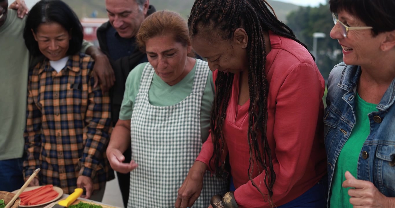 Felice gruppo multietnico di anziani che prepara cibo all'aperto
