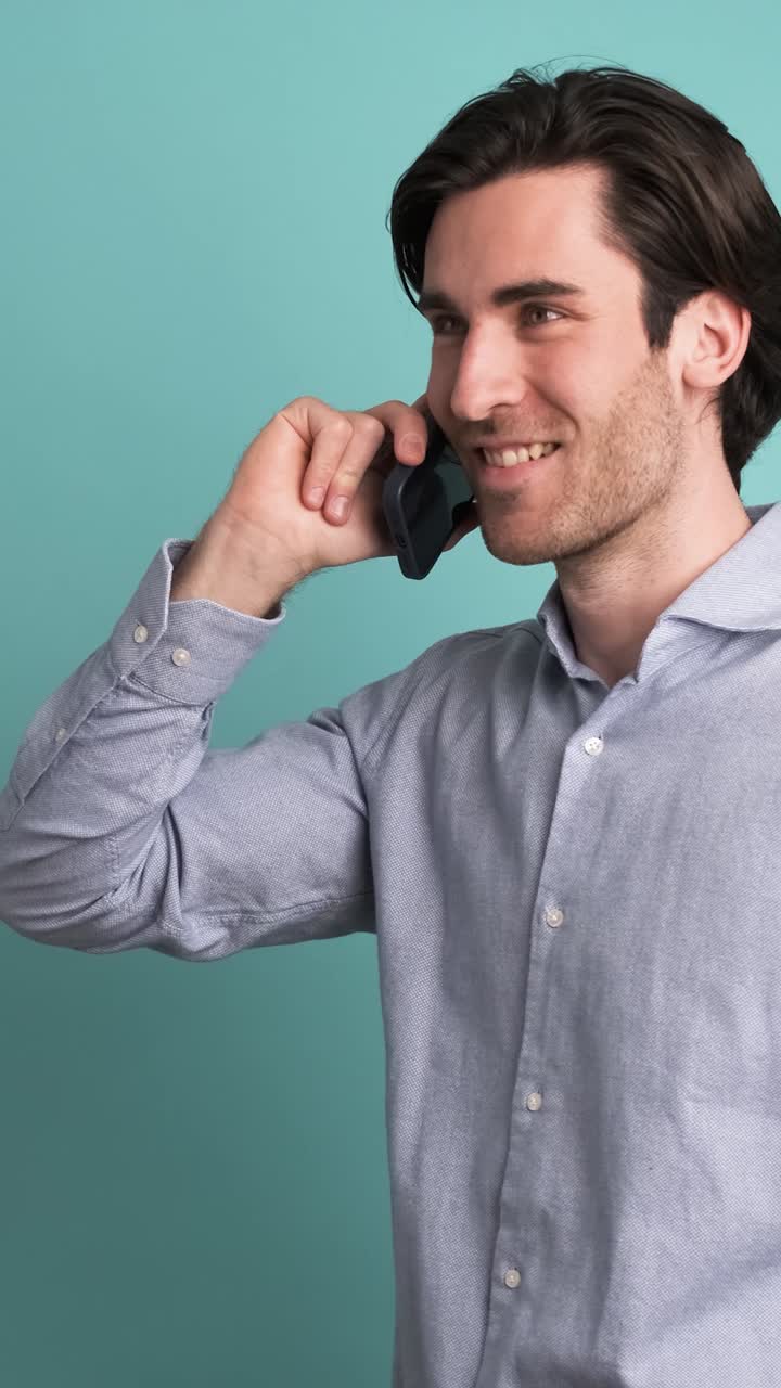 Smiling adult man talking on smartphone in blue studio