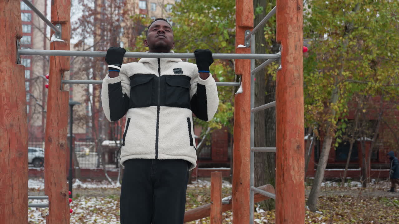 joven realizando ejercicios de tracción en una barra de entrenamiento al aire libre en invierno, vestido con una cálida chaqueta de lana y guantes, agarra la barra con determinación