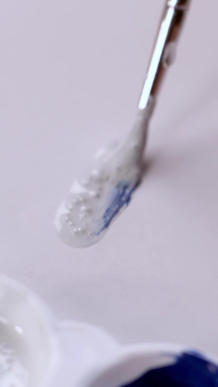 Close-up of brush blending blue and white paint on palette, soft lighting, smooth camera movement